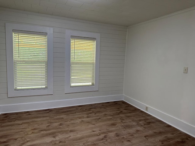 spare room featuring dark hardwood / wood-style flooring, a wealth of natural light, ornamental molding, and wood walls