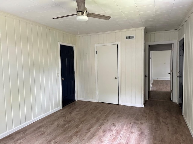 unfurnished bedroom featuring hardwood / wood-style floors, a closet, ceiling fan, and wooden walls