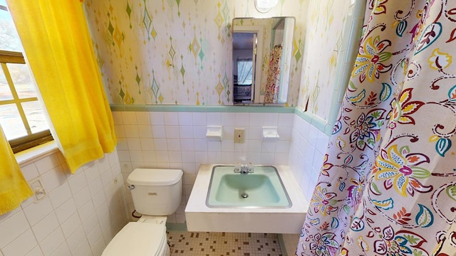 full bath featuring a wainscoted wall, toilet, curtained shower, a sink, and wallpapered walls