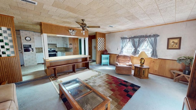 living area featuring visible vents, ceiling fan, wood walls, and wainscoting