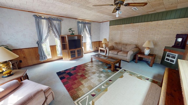 living area with crown molding, carpet, wooden walls, a ceiling fan, and wainscoting