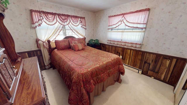 bedroom featuring a wainscoted wall, wallpapered walls, baseboard heating, and light colored carpet