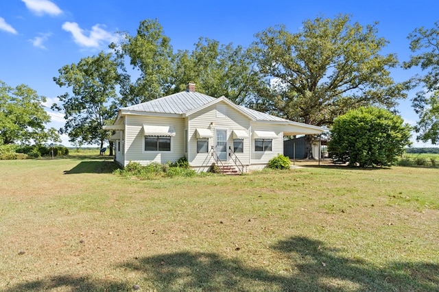 back of house with entry steps, a chimney, metal roof, and a yard