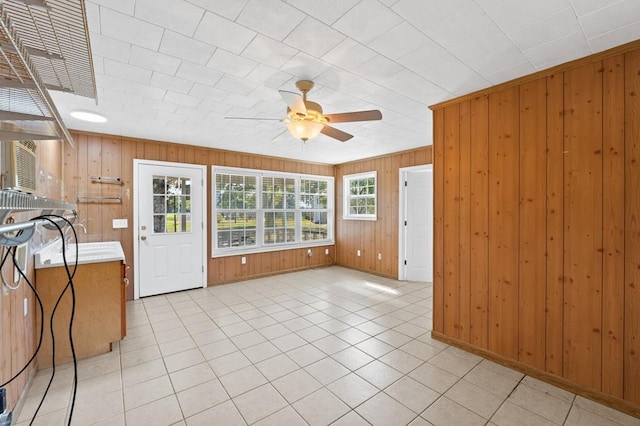 empty room featuring ceiling fan, light tile patterned floors, and wood walls