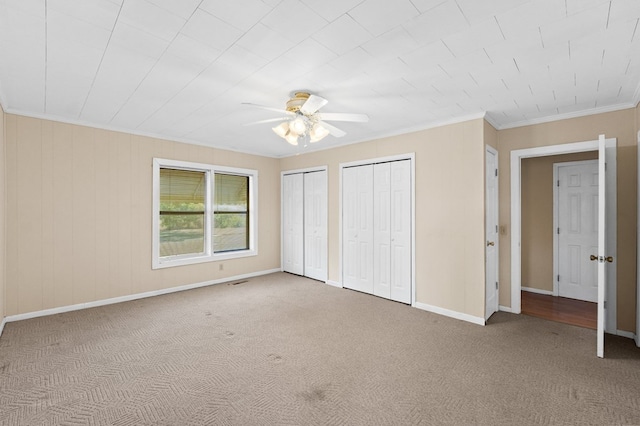 unfurnished bedroom with carpet floors, two closets, ornamental molding, ceiling fan, and baseboards