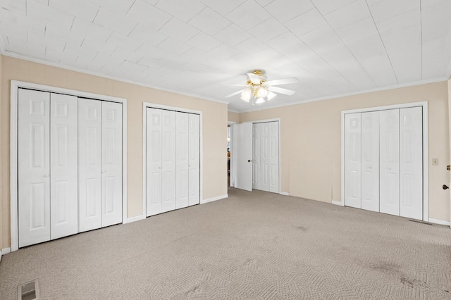 unfurnished bedroom with baseboards, visible vents, crown molding, carpet floors, and multiple closets