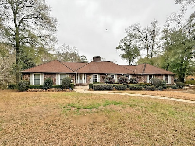 ranch-style house featuring a front yard, brick siding, and a chimney