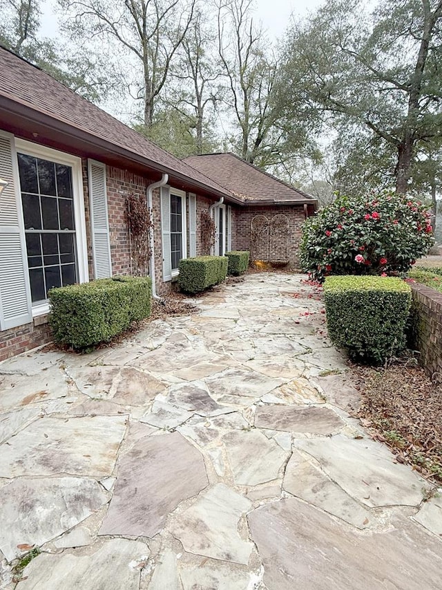 view of side of property featuring a shingled roof, a patio, and brick siding