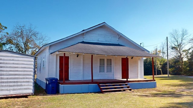 back of house featuring covered porch, a yard, and a shingled roof