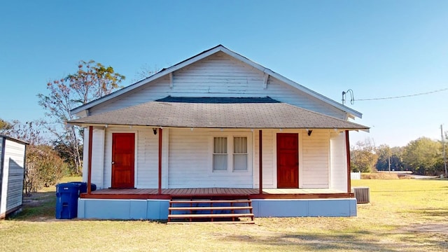 view of front of house with a shingled roof, covered porch, and a front lawn
