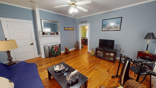 living room featuring visible vents, baseboards, a ceiling fan, crown molding, and light wood-style floors