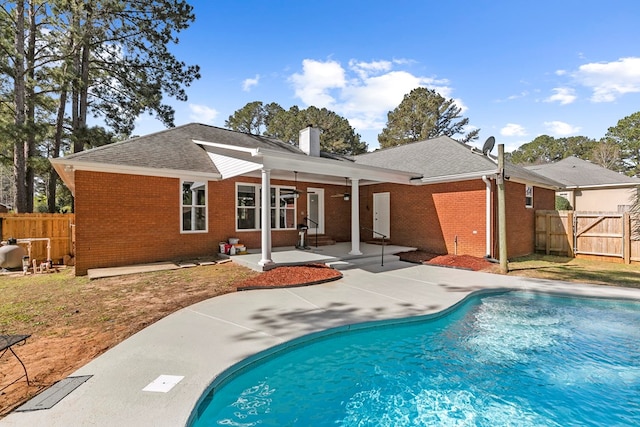 rear view of house featuring brick siding, a fenced in pool, a chimney, a patio area, and a ceiling fan