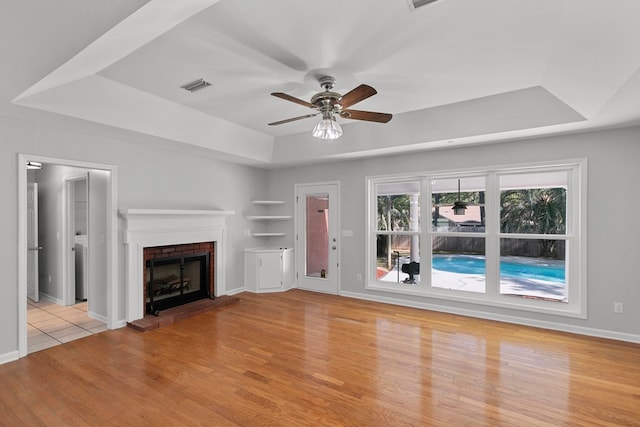 unfurnished living room featuring a tray ceiling, a brick fireplace, light wood-style floors, and visible vents