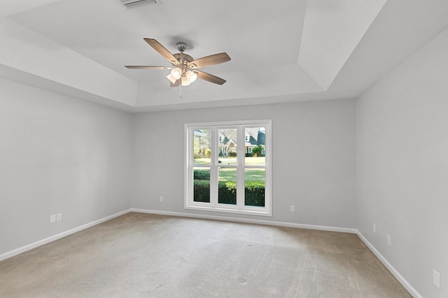 carpeted empty room featuring a tray ceiling, baseboards, and ceiling fan