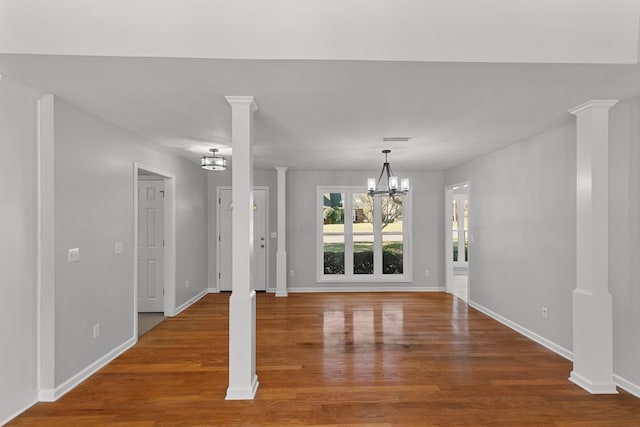 interior space featuring an inviting chandelier, baseboards, ornate columns, and wood finished floors