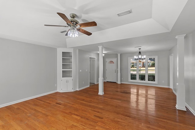 unfurnished living room featuring built in shelves, wood finished floors, visible vents, decorative columns, and ceiling fan with notable chandelier