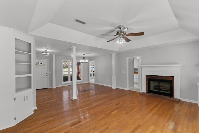 unfurnished living room featuring visible vents, a brick fireplace, light wood-type flooring, and a tray ceiling