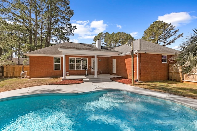 back of property with brick siding, a fenced in pool, fence, a chimney, and a patio