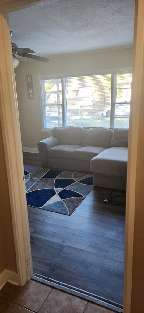 living room with ceiling fan, wood finished floors, baseboards, and a textured ceiling