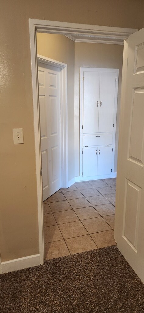 hallway featuring light tile patterned floors, baseboards, and ornamental molding