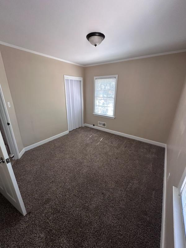 carpeted empty room featuring visible vents, baseboards, and crown molding