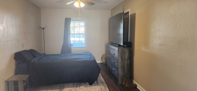 bedroom featuring ceiling fan, baseboards, dark wood finished floors, and a textured wall