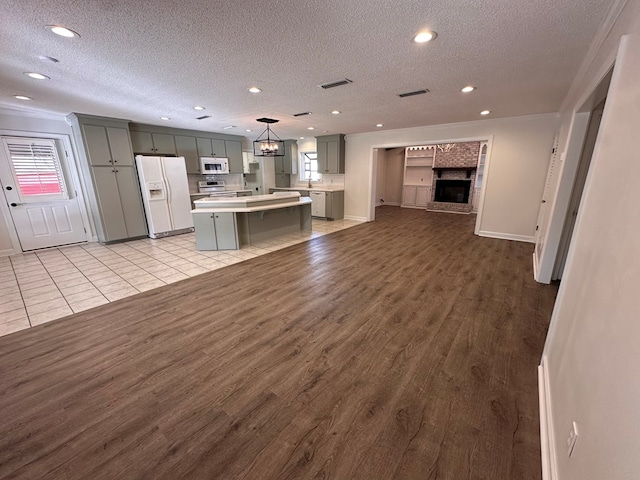 kitchen with hanging light fixtures, gray cabinetry, a kitchen breakfast bar, white appliances, and a center island