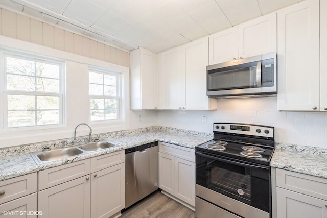 kitchen with sink, light stone counters, light hardwood / wood-style floors, white cabinets, and appliances with stainless steel finishes