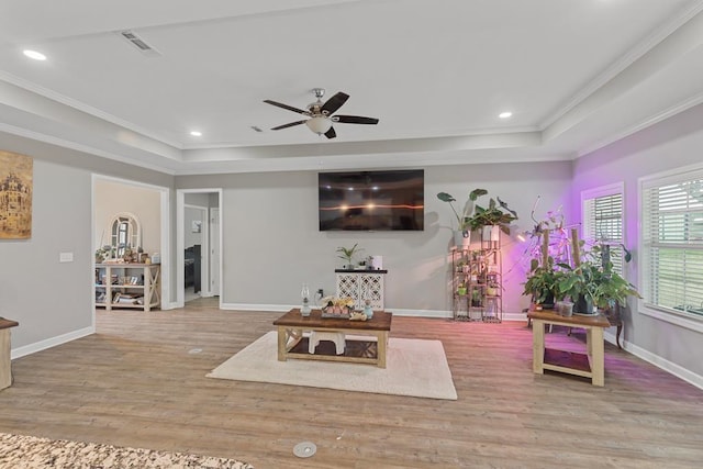 living room with hardwood / wood-style flooring, ceiling fan, crown molding, and a raised ceiling