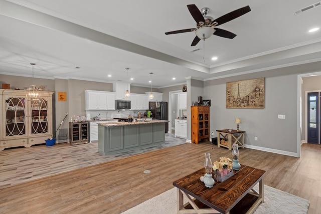 living room with ceiling fan with notable chandelier, beverage cooler, ornamental molding, a raised ceiling, and light hardwood / wood-style flooring