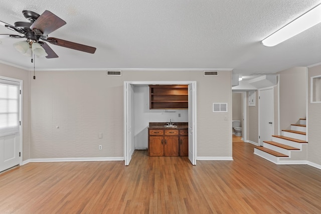 unfurnished living room with sink, crown molding, a textured ceiling, light wood-type flooring, and ceiling fan