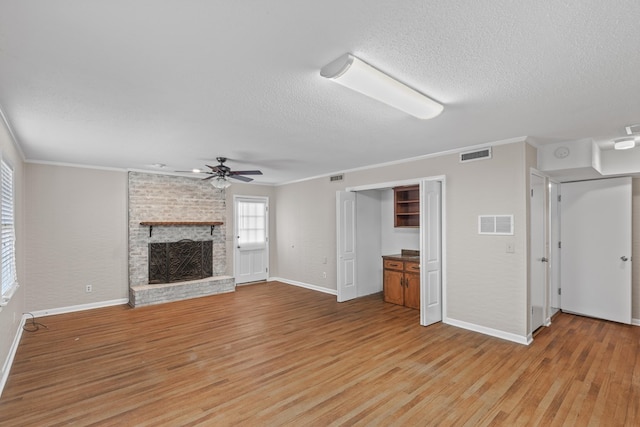 unfurnished living room featuring crown molding, ceiling fan, light hardwood / wood-style floors, a textured ceiling, and a brick fireplace