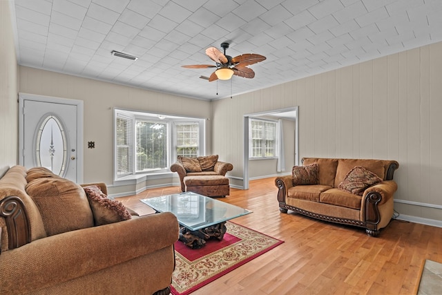 living room with ceiling fan, wood walls, and wood-type flooring