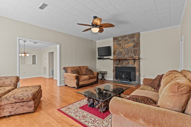 living room featuring hardwood / wood-style flooring, ceiling fan with notable chandelier, a wood stove, and crown molding