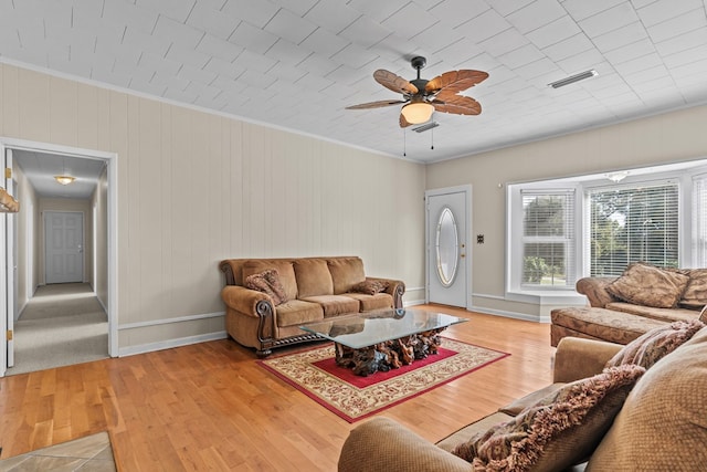 living room featuring ceiling fan, light hardwood / wood-style floors, ornamental molding, and wooden walls