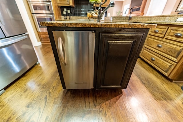 room details featuring tasteful backsplash, dark brown cabinets, stainless steel appliances, and hardwood / wood-style flooring