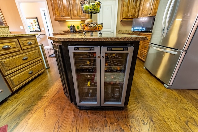 bar featuring stainless steel fridge, light stone counters, beverage cooler, and dark wood-type flooring