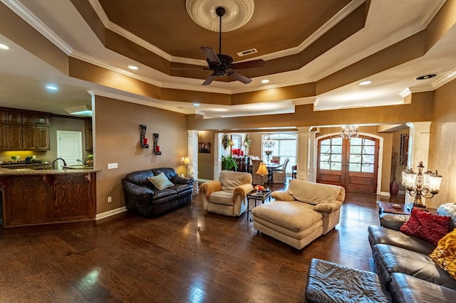 living room featuring dark hardwood / wood-style floors, ornate columns, ornamental molding, and a tray ceiling