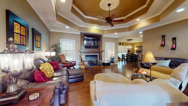 living room featuring ceiling fan, a raised ceiling, crown molding, and dark wood-type flooring