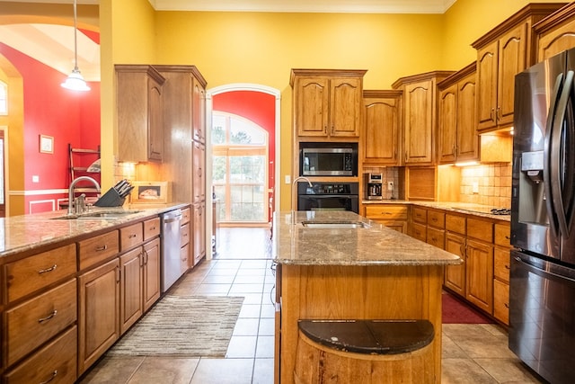 kitchen with light stone countertops, sink, light tile patterned floors, a kitchen island, and appliances with stainless steel finishes