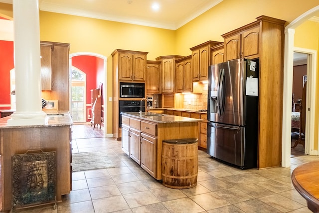 kitchen with stainless steel appliances, tasteful backsplash, decorative columns, a center island with sink, and ornamental molding