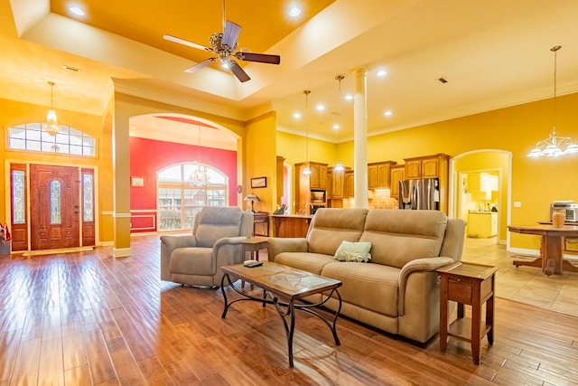 living room featuring ceiling fan with notable chandelier, crown molding, a high ceiling, and light hardwood / wood-style flooring