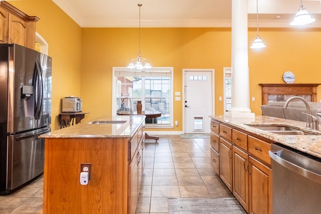 kitchen featuring sink, hanging light fixtures, stainless steel appliances, decorative columns, and an island with sink