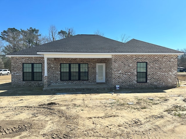 rear view of house featuring brick siding and roof with shingles