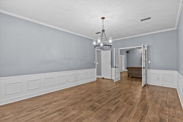unfurnished dining area featuring a wainscoted wall, ornamental molding, a notable chandelier, and wood finished floors