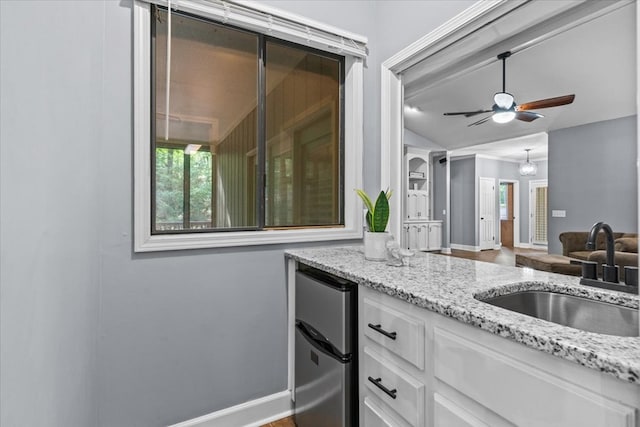 kitchen with a sink, ceiling fan, light stone counters, white cabinets, and freestanding refrigerator