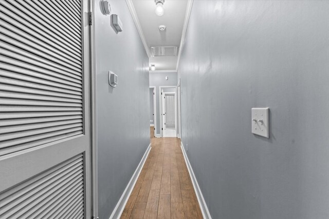 hallway featuring attic access, hardwood / wood-style flooring, ornamental molding, and baseboards