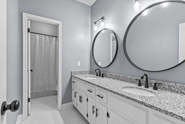 bathroom with baseboards, tile patterned flooring, double vanity, and a sink
