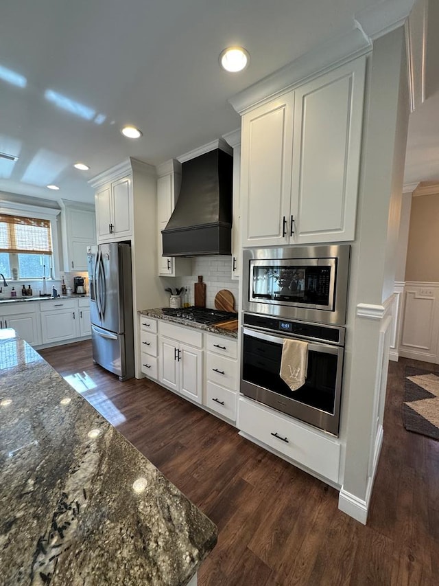 kitchen with premium range hood, ornamental molding, appliances with stainless steel finishes, and white cabinets