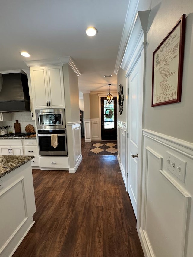 hall featuring recessed lighting, a wainscoted wall, dark wood-style floors, a decorative wall, and crown molding